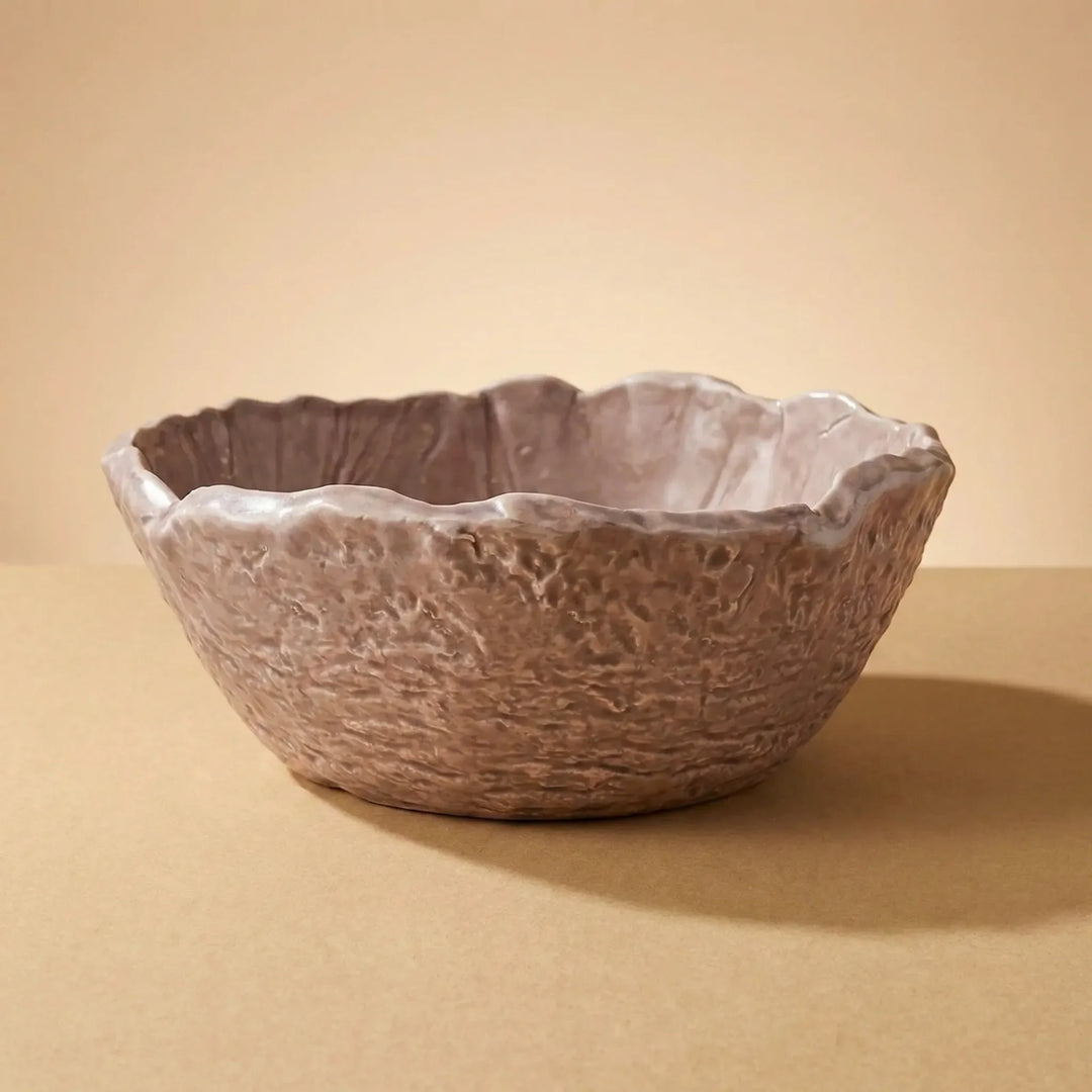 Ciotola artigianale in ceramica marrone con bordo irregolare e texture materica su sfondo neutro