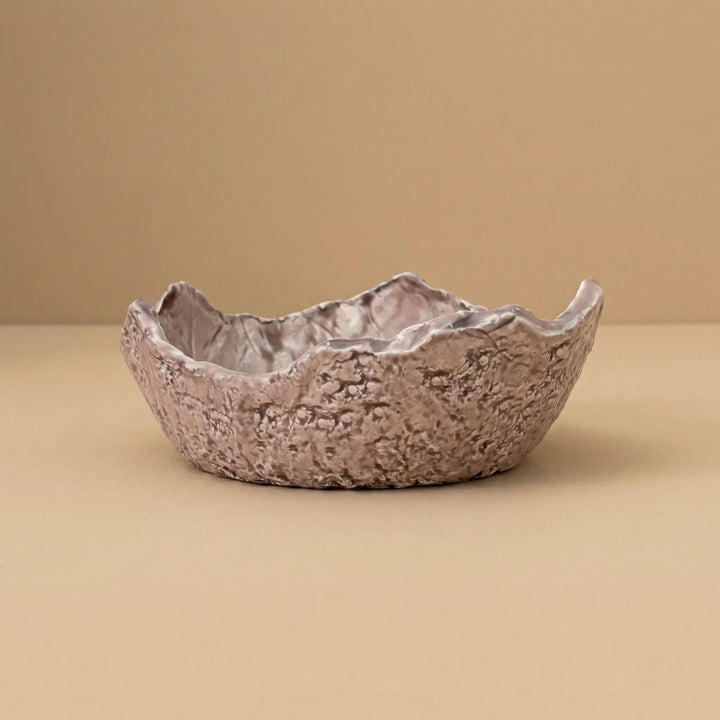 Ciotola in ceramica artigianale con bordo irregolare e texture naturale su sfondo neutro beige