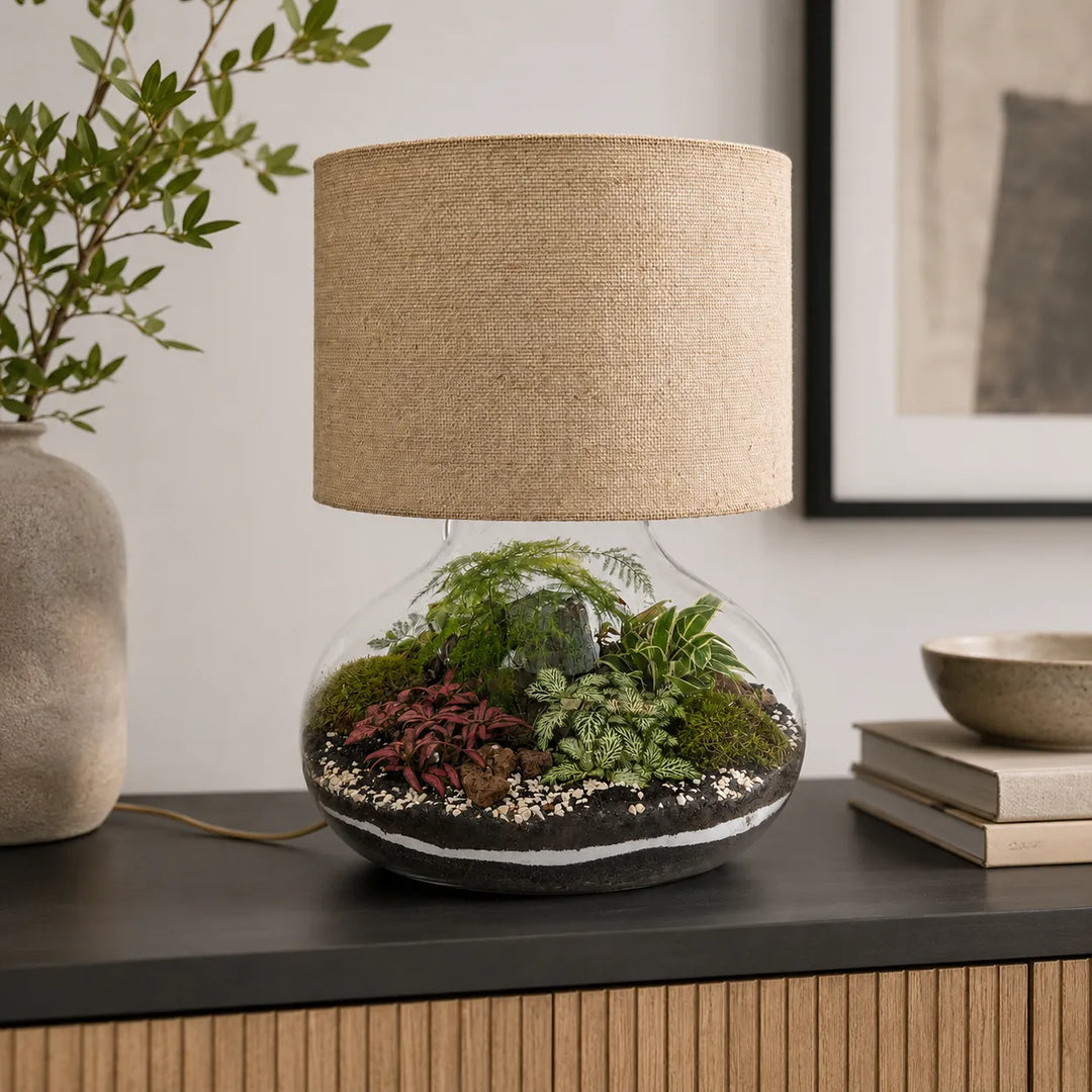 Lamparium Flora XXL con paralume in juta collocato su una madia moderna, terrarium artigianale in vetro con piante decorative per arredare la casa.