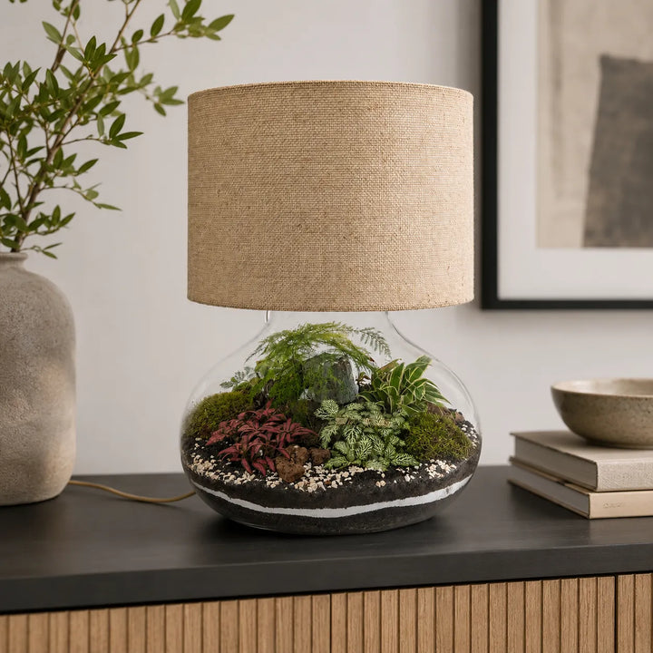 Lamparium Flora XXL con paralume in juta collocato su una madia moderna, terrarium artigianale in vetro con piante decorative per arredare la casa.