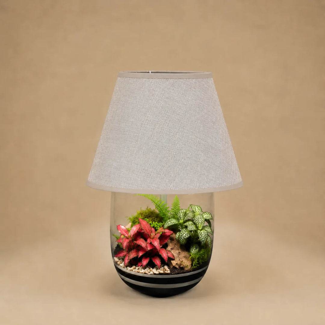 Terrarium artigianale Oasi Lux Elegant con piante tropicali da interno racchiuse in una lampada decorativa con paralume beige e vaso in vetro.
